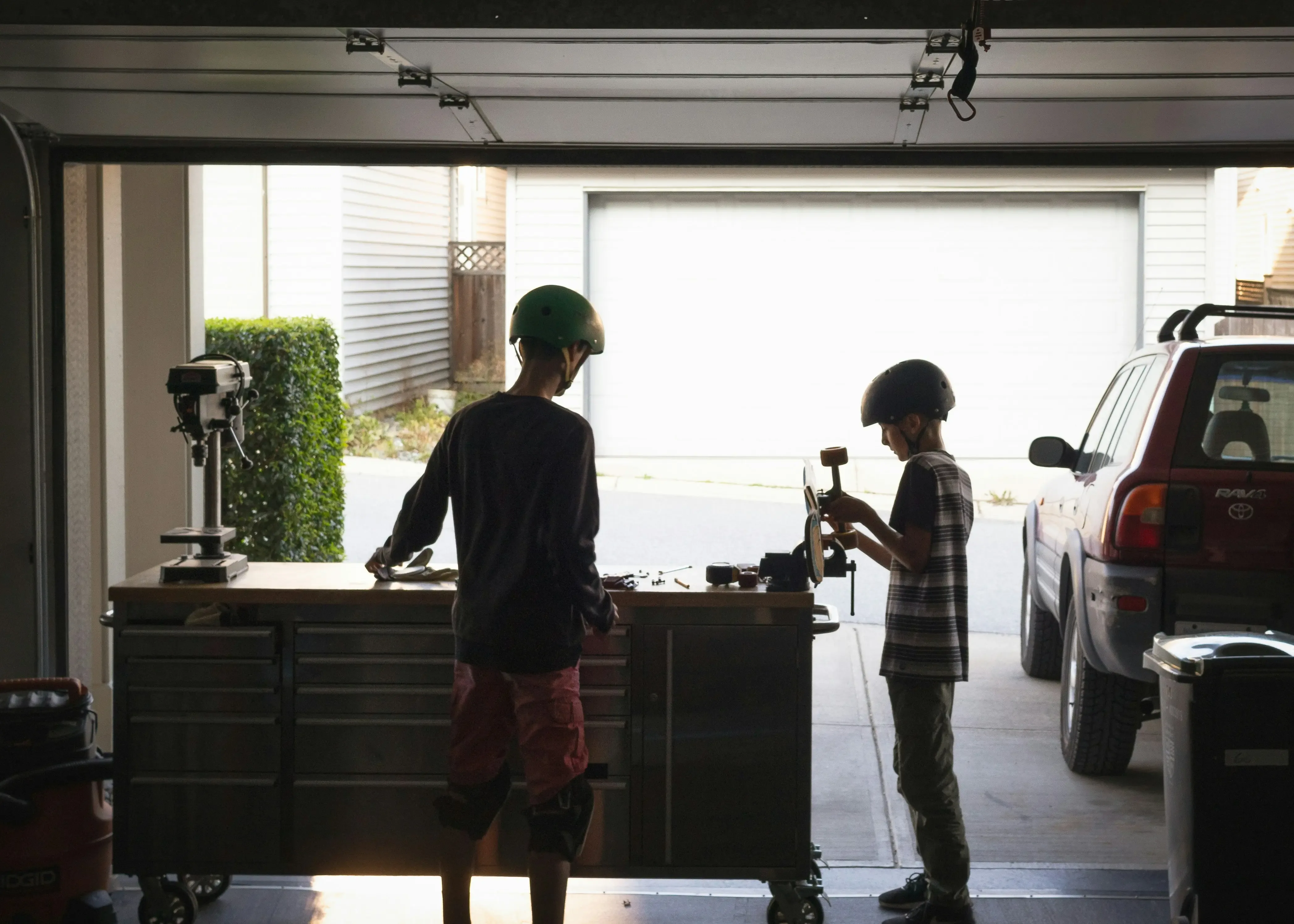 Deux jeunes travaillent sur la réparation ou l'entretien d'un skateboard dans un garage résidentiel